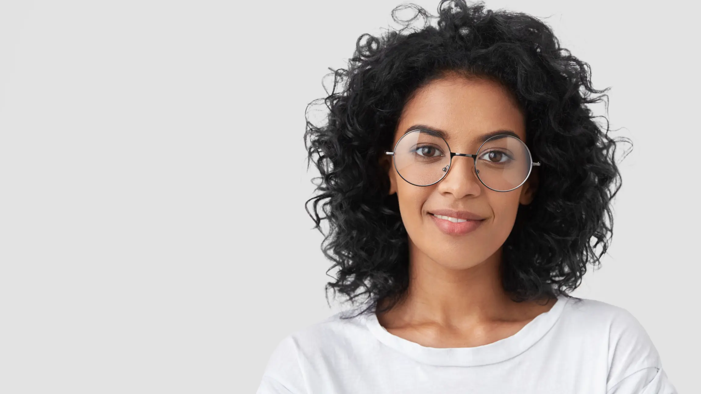 A woman with dark, curly hair and glasses looks smiling into the camera.