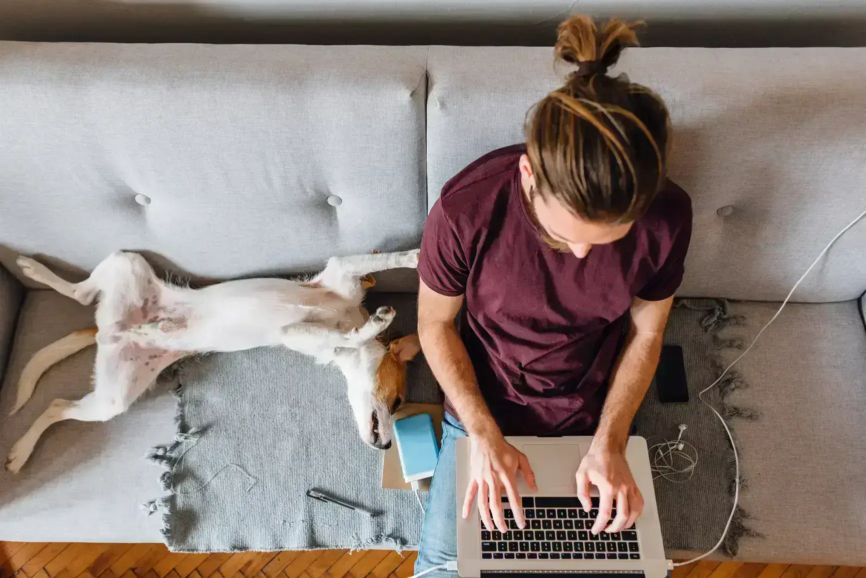 A man works on his laptop while his dog lies next to him on his back