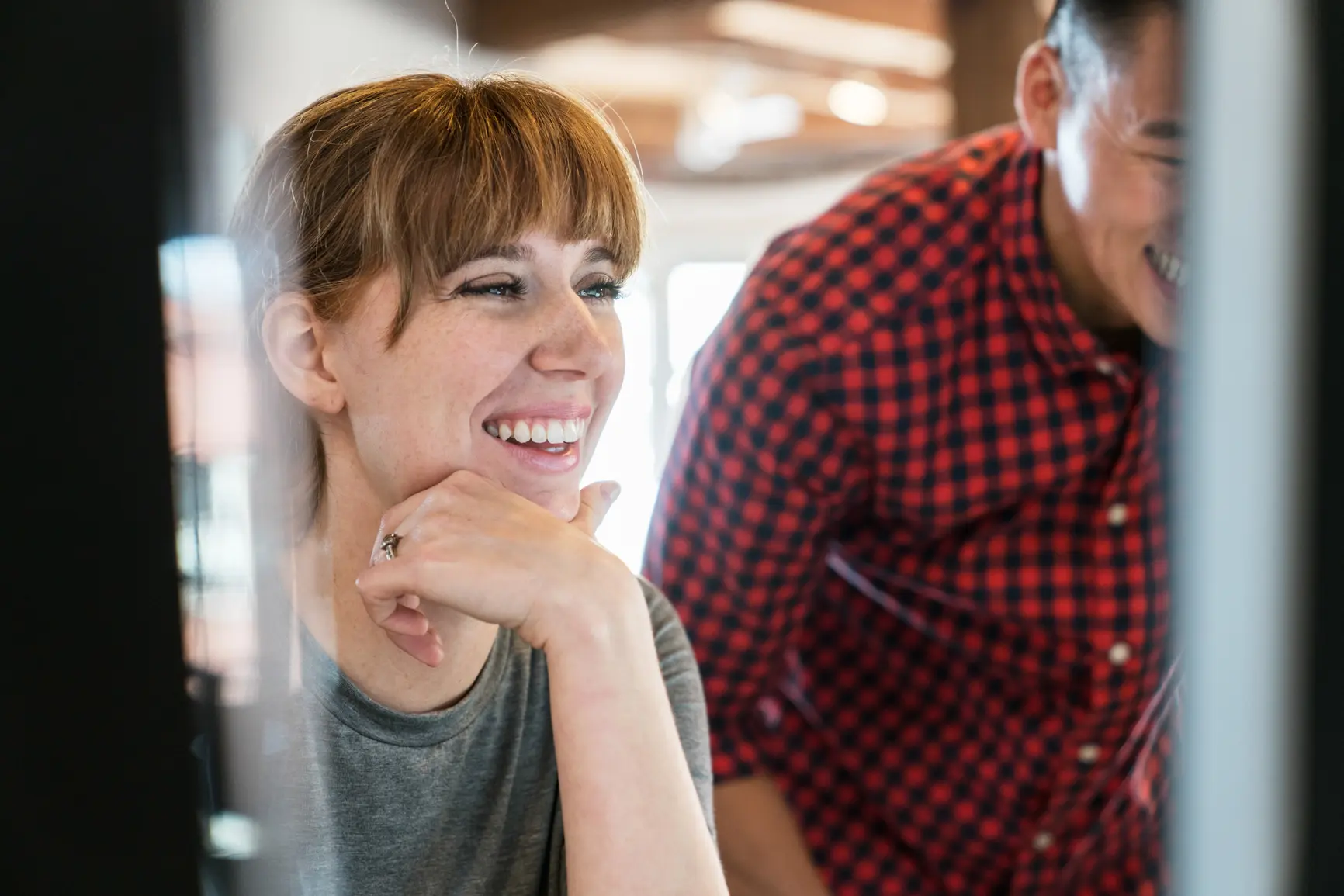 Two young businessmen laugh while looking at a screen.