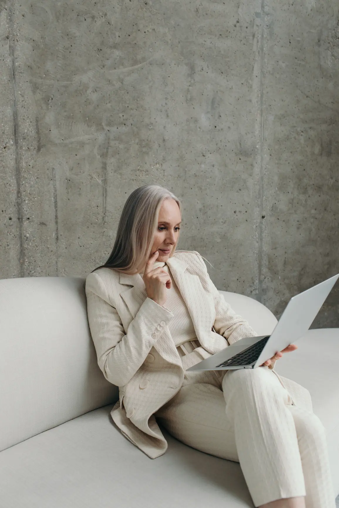 An elderly businesswoman works on her laptop while sitting on the sofa.