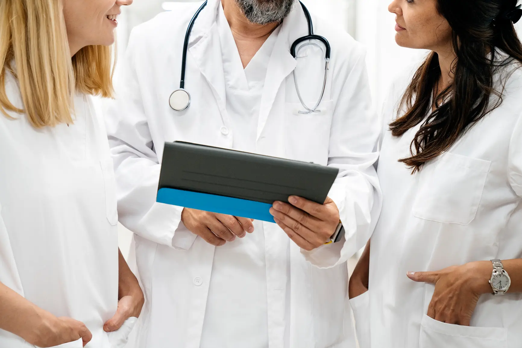 Three physicians review a patient's treatment history on a tablet.