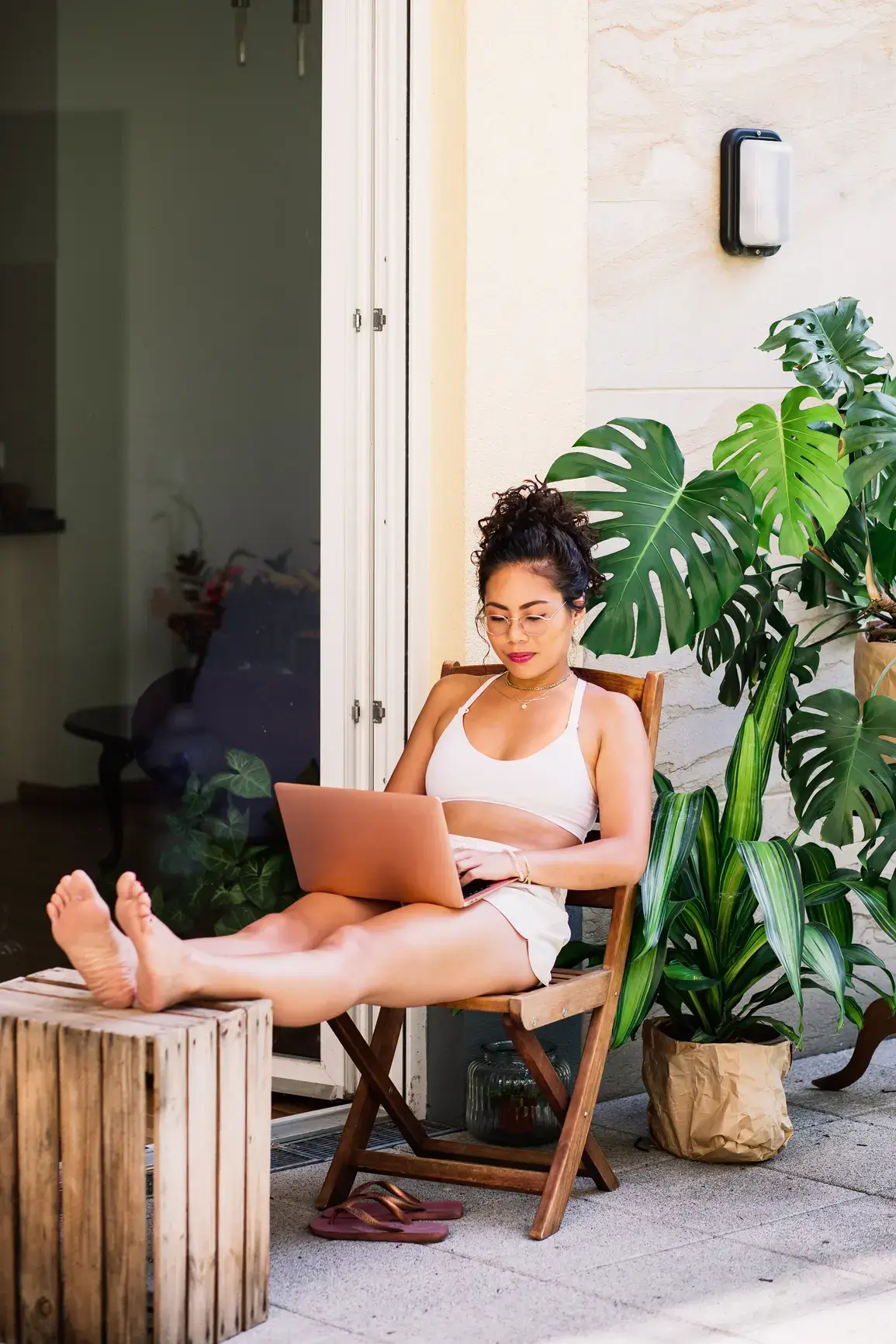 A woman works with her feet up on her terrace. In the background you can see many plants.