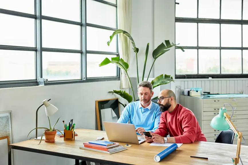 Two architects are sitting in a bright office at their laptops, planning a project.