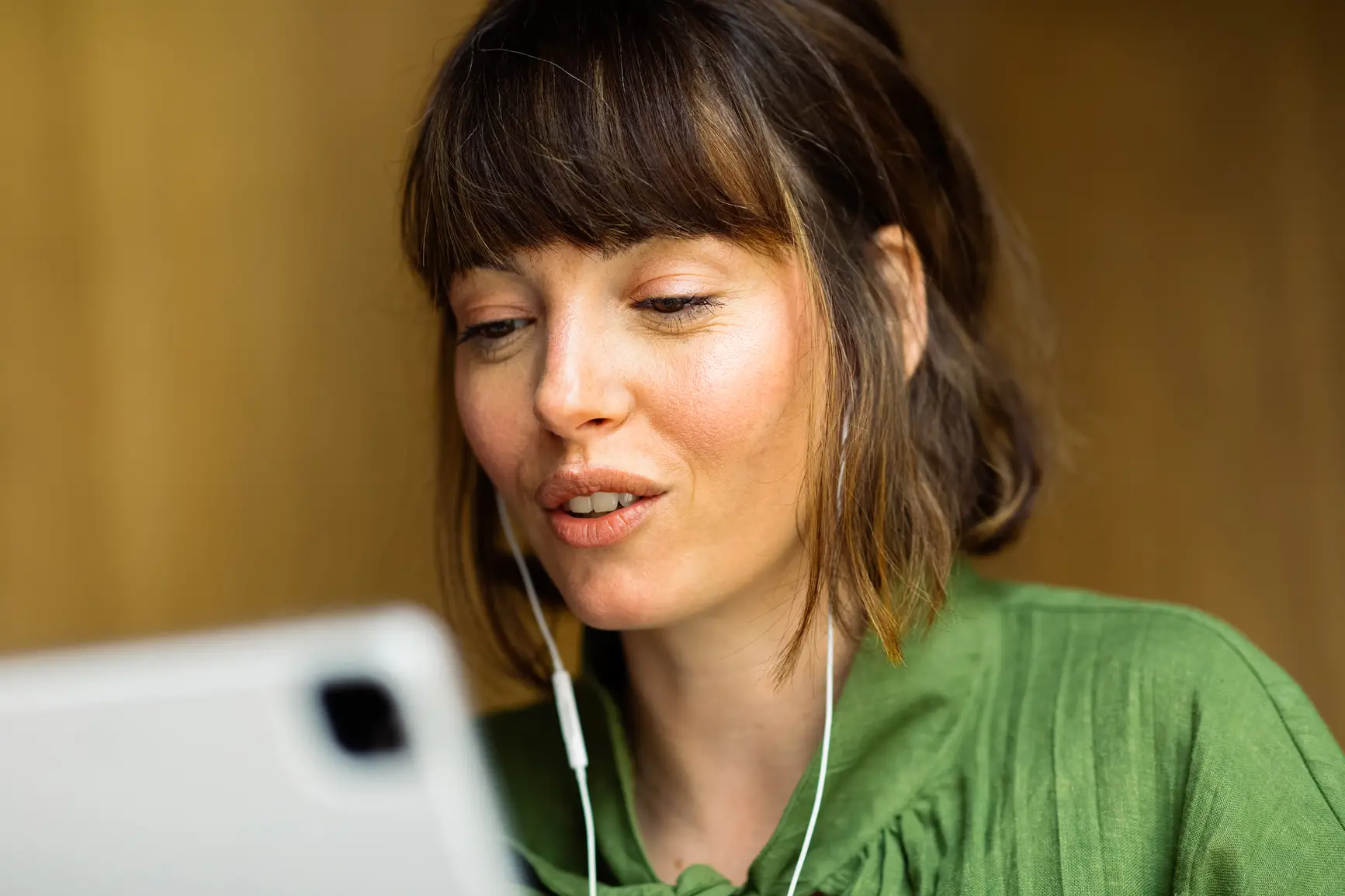 Woman with earphones engaged in a video or voice call on a tablet. She is wearing a green blouse and appears focused during the conversation.