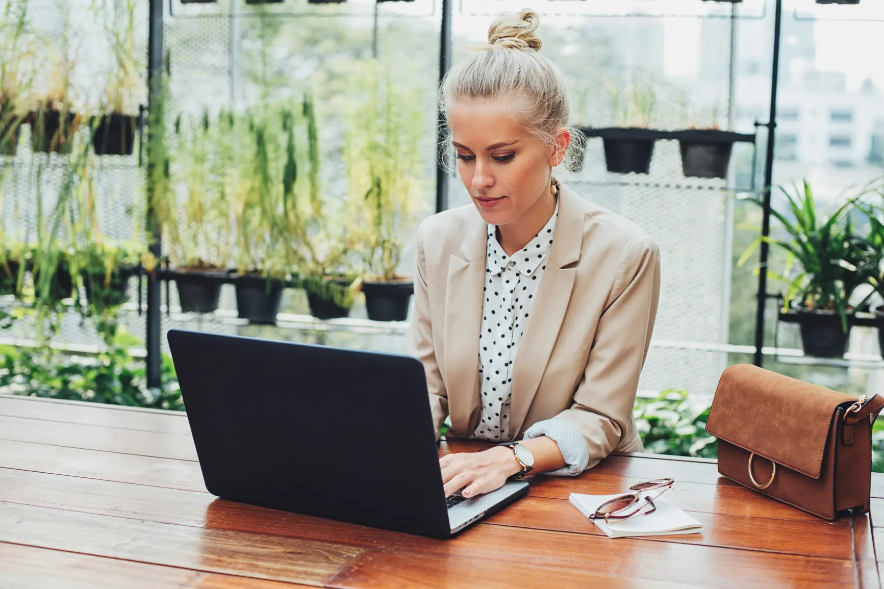 Frau in einem modernen, begrünten Arbeitsumfeld nutzt ihren Laptop für eine Online-Besprechung.