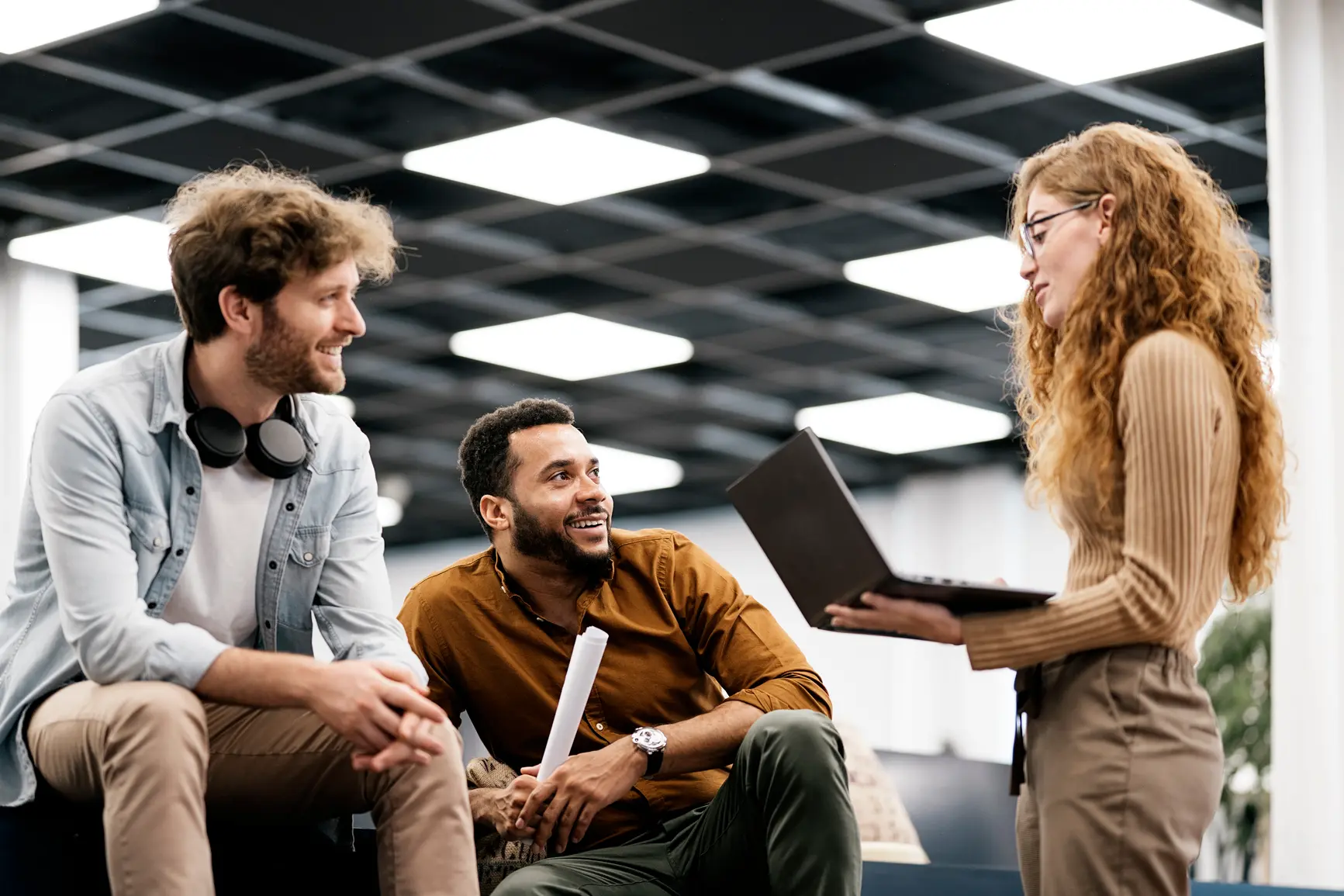 A woman with a laptop in her hand is talking to her two colleagues.