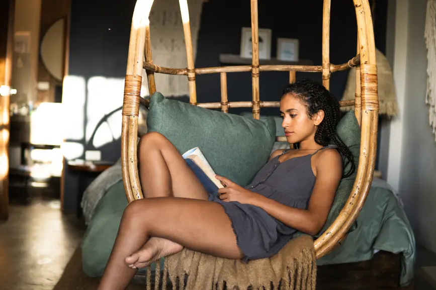 Eine Frau liest gemuetlich ein Buch zuhause in ihrem Haengesessel.