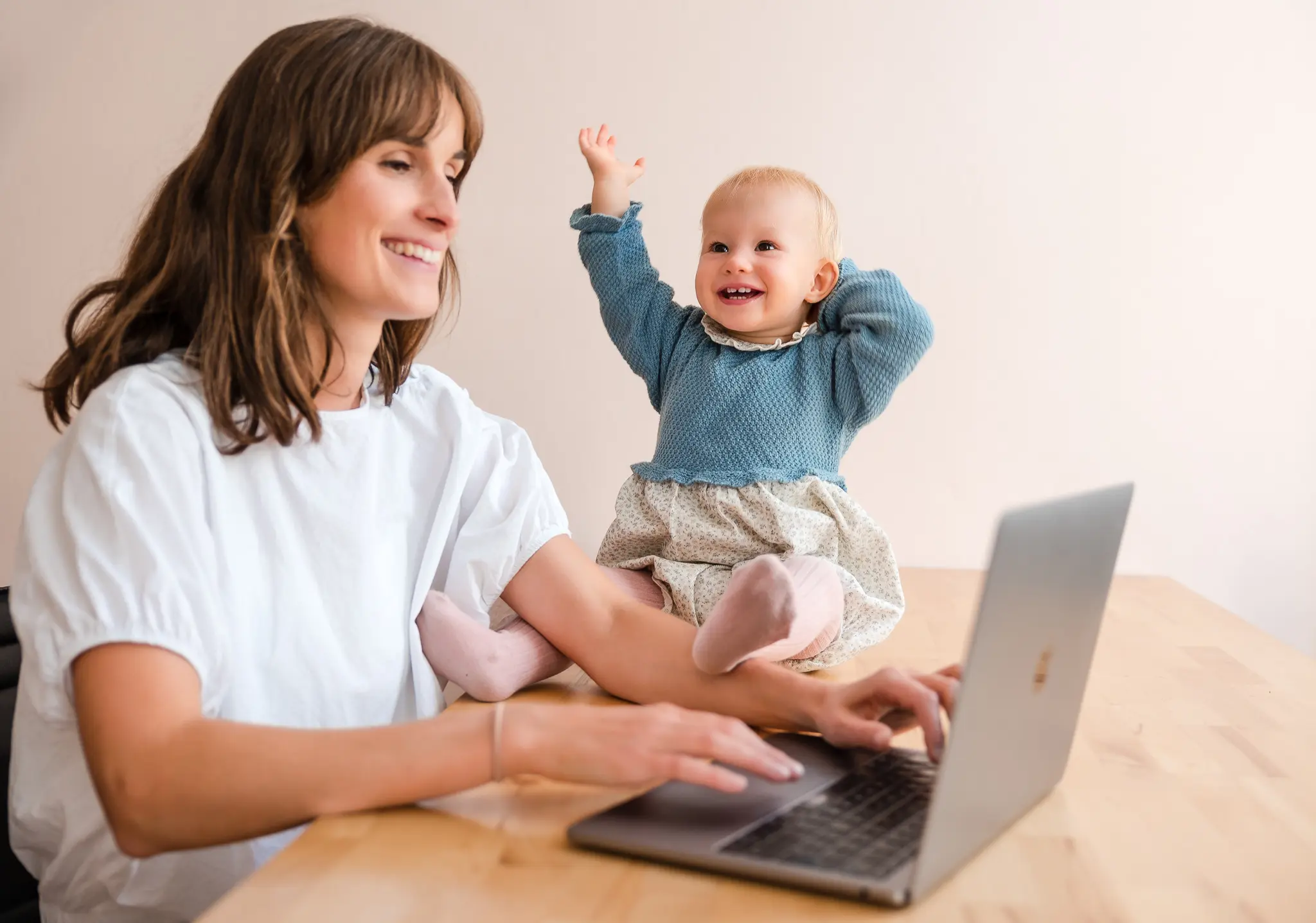 Happy woman sits in front of PC together with her laughing child.