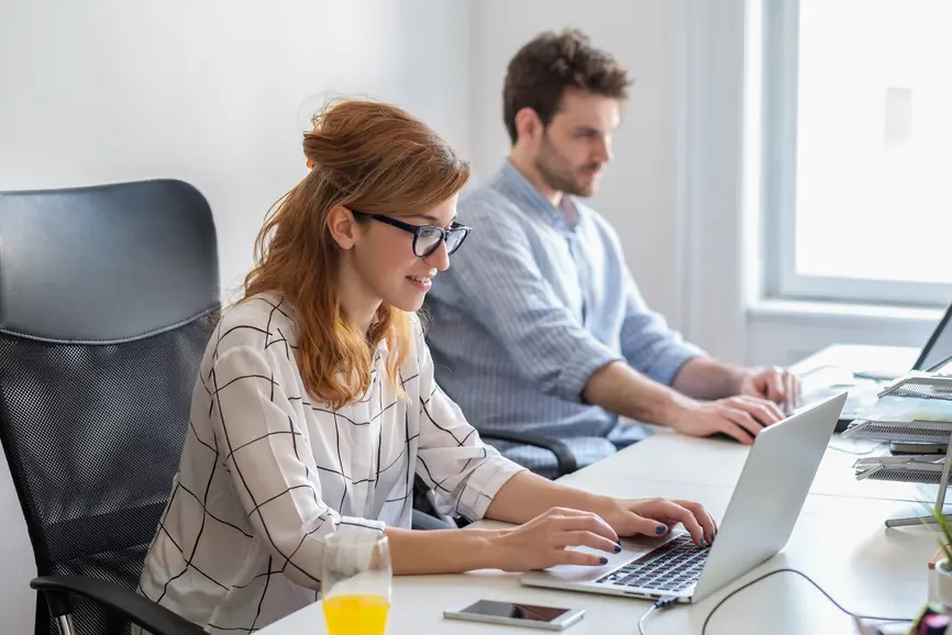 Eine Frau und ein Mann sitzen im Buero und arbeiten an ihren Laptops.