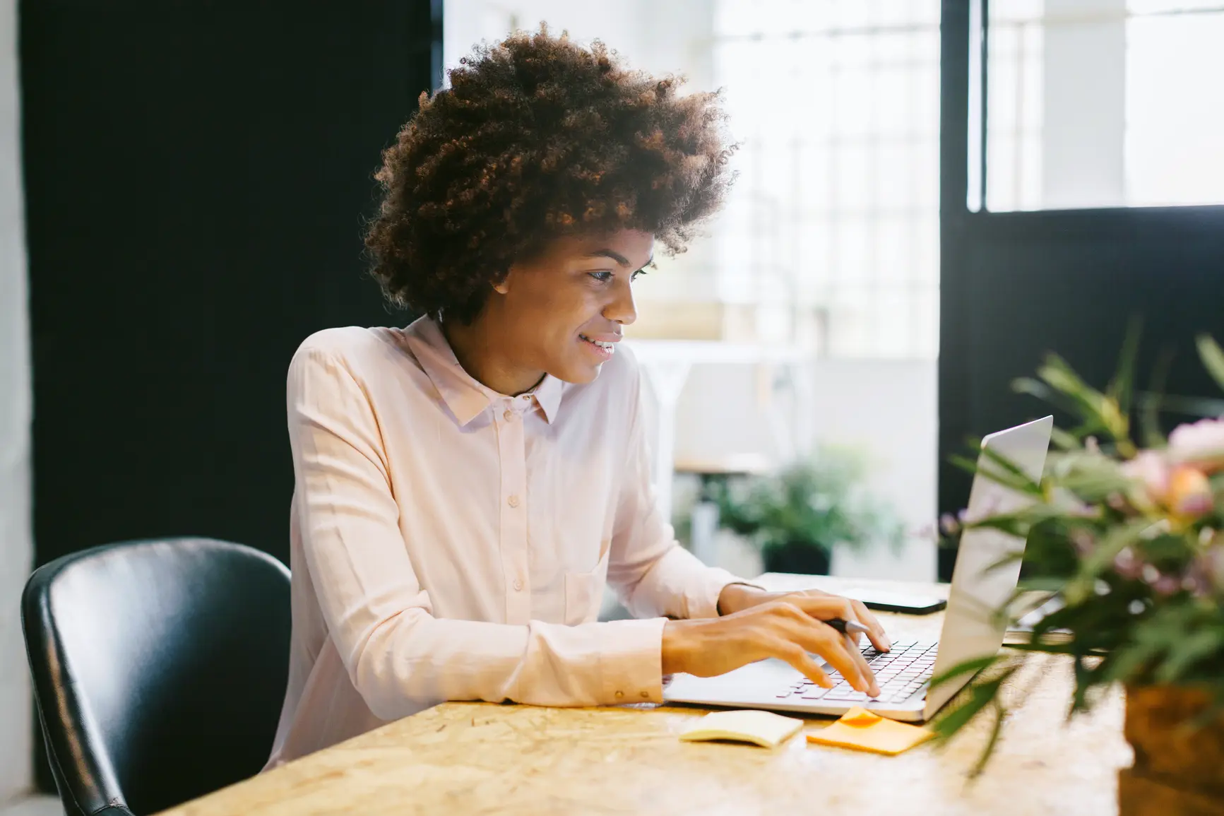 A businesswoman in a bright blouse is writing an email at her desk.