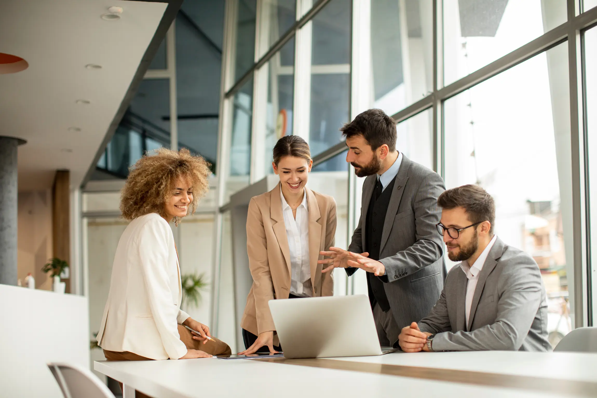 Four colleagues in professional attire work in a large, open office.