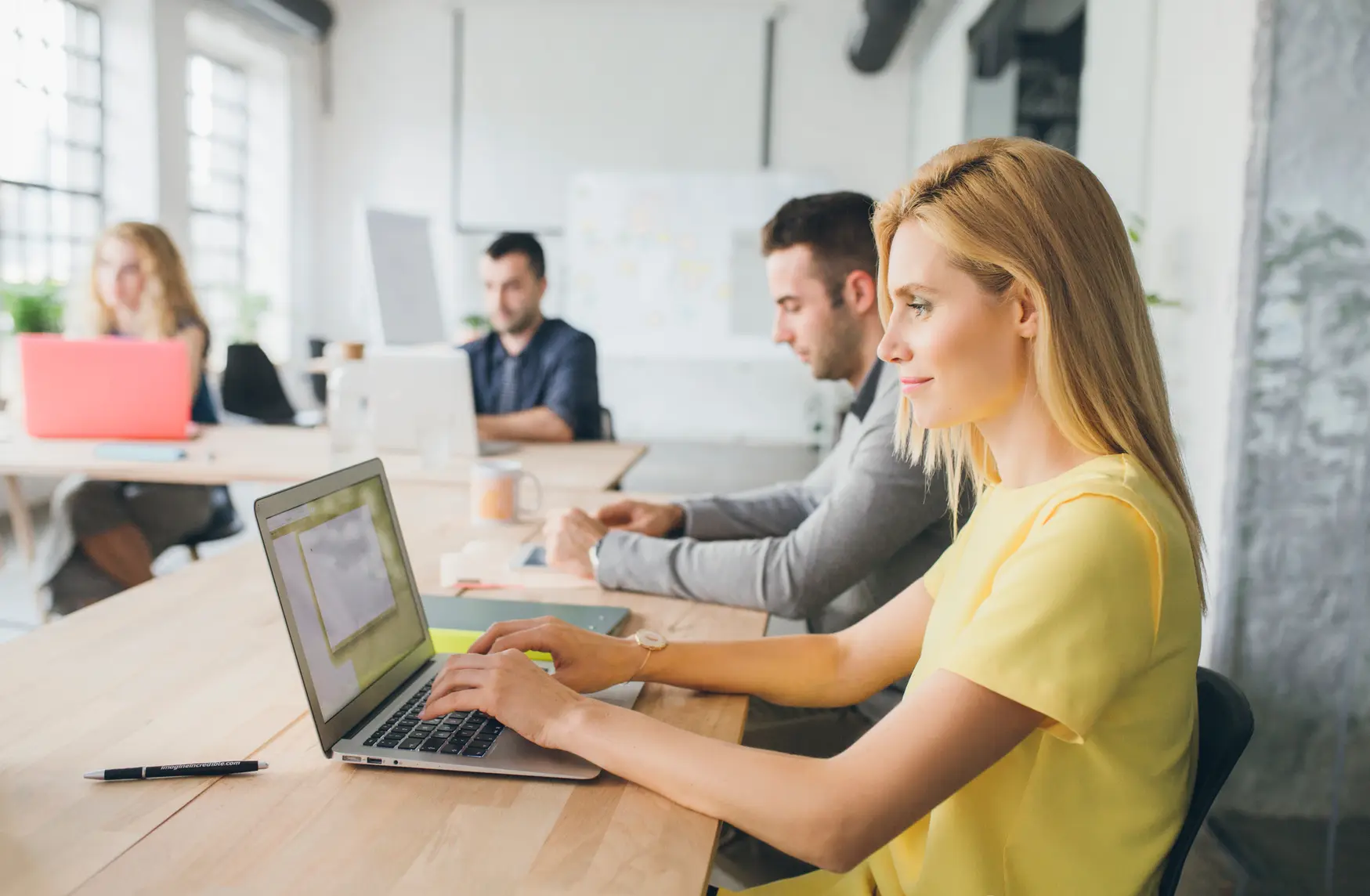 Vier Personen sitzen an einem L-foermigen Tisch und arbeiten an Laptops und auf Papier.