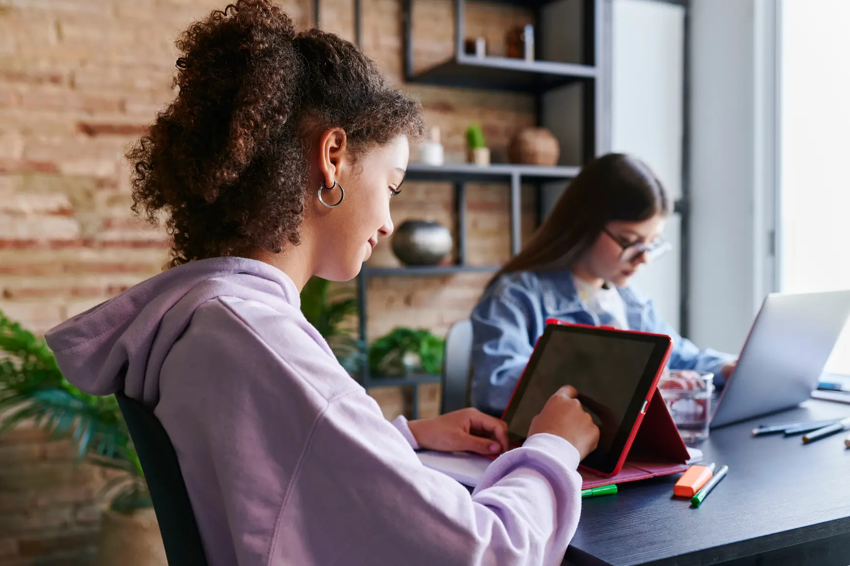 Zwei Schuelerinnen machen gemeinsam Hausaufgaben an Tablet und Laptop.