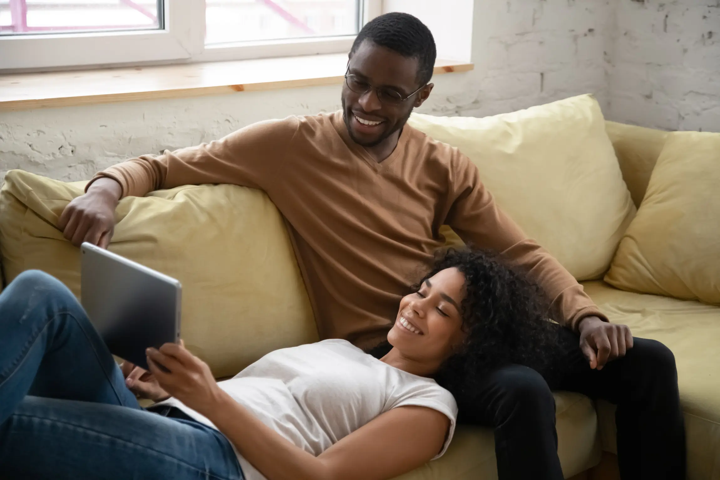 A young couple sits together on the sofa and watches a video on the tablet.