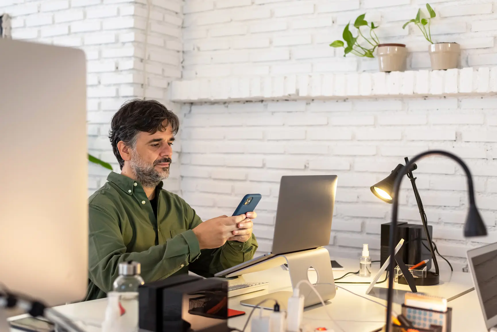 A man at a desk is typing something into his smartphone.