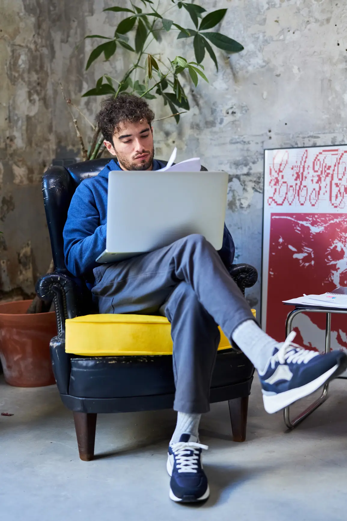 Ein junger Programmierer sitzt mit seinem Laptop in einem Sessel und liest eine Anleitung.