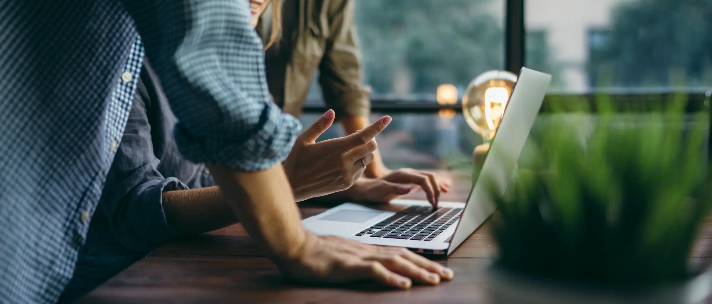 Ausschnitt einer Arbeitssituation: Vor einem Laptop stehen eine Frau und ein Mann. Zu sehen sind ihre Haende und Oberkoerper.