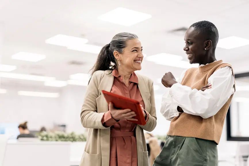 A woman shows a new employee the results of a project on a tablet.