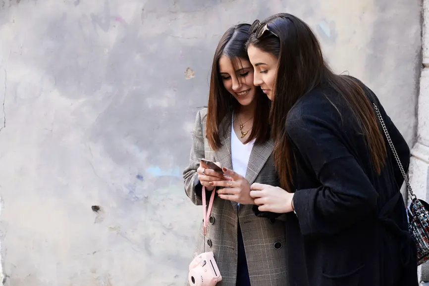 Zwei Freundinnen schauen im Freien auf ein Smartphone.