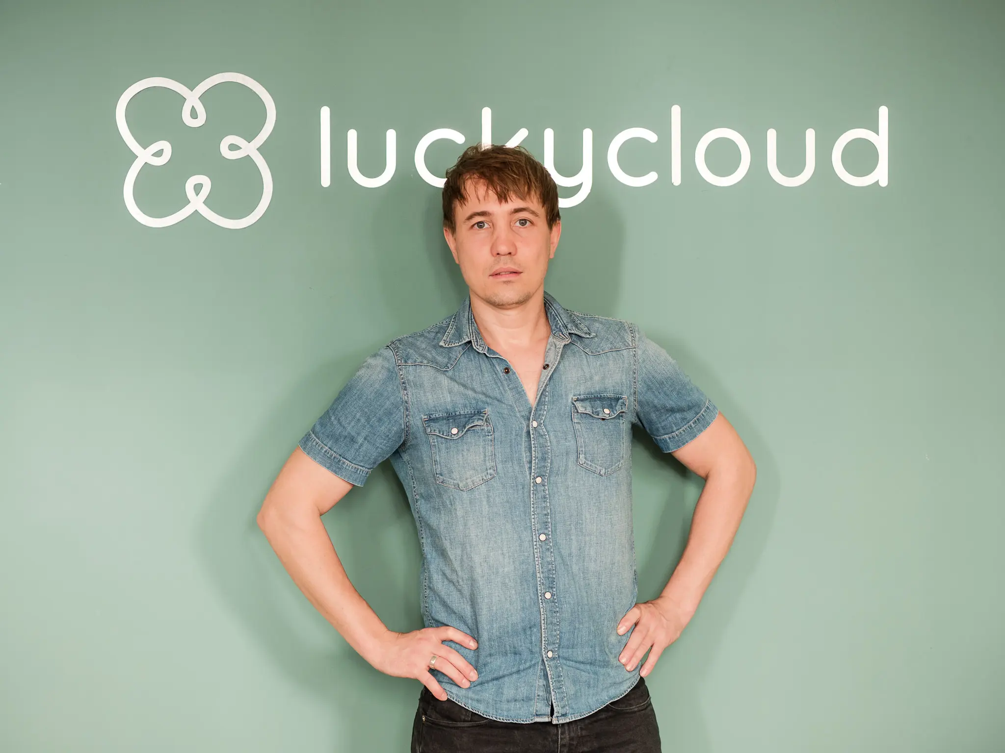 The founder of luckycloud poses with his hands in his hips in front of the logo and lettering.