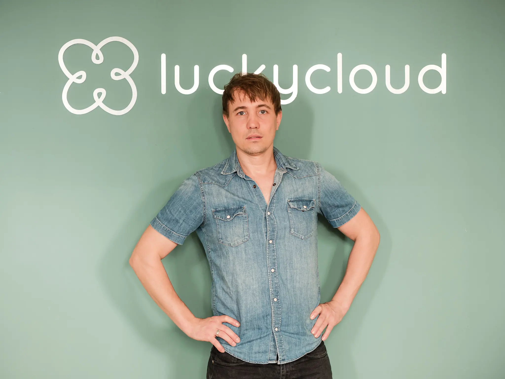 Der Gruender von luckycloud posiert mit den Haenden in der Huefte vor dem Logo und Schriftzug.