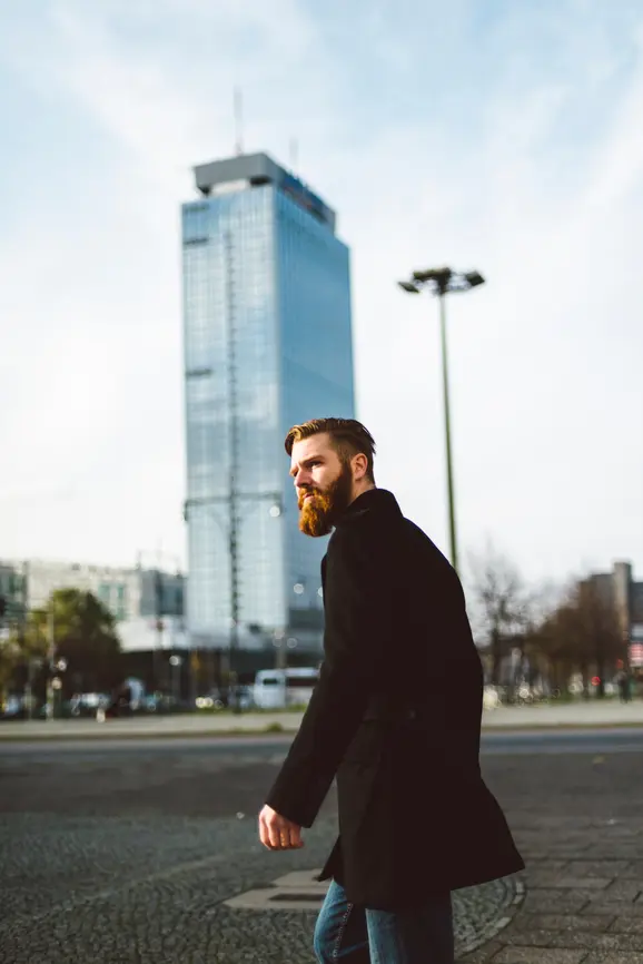 A man with a beard stands on a street in Berlin, in the background you can see a skyscraper.