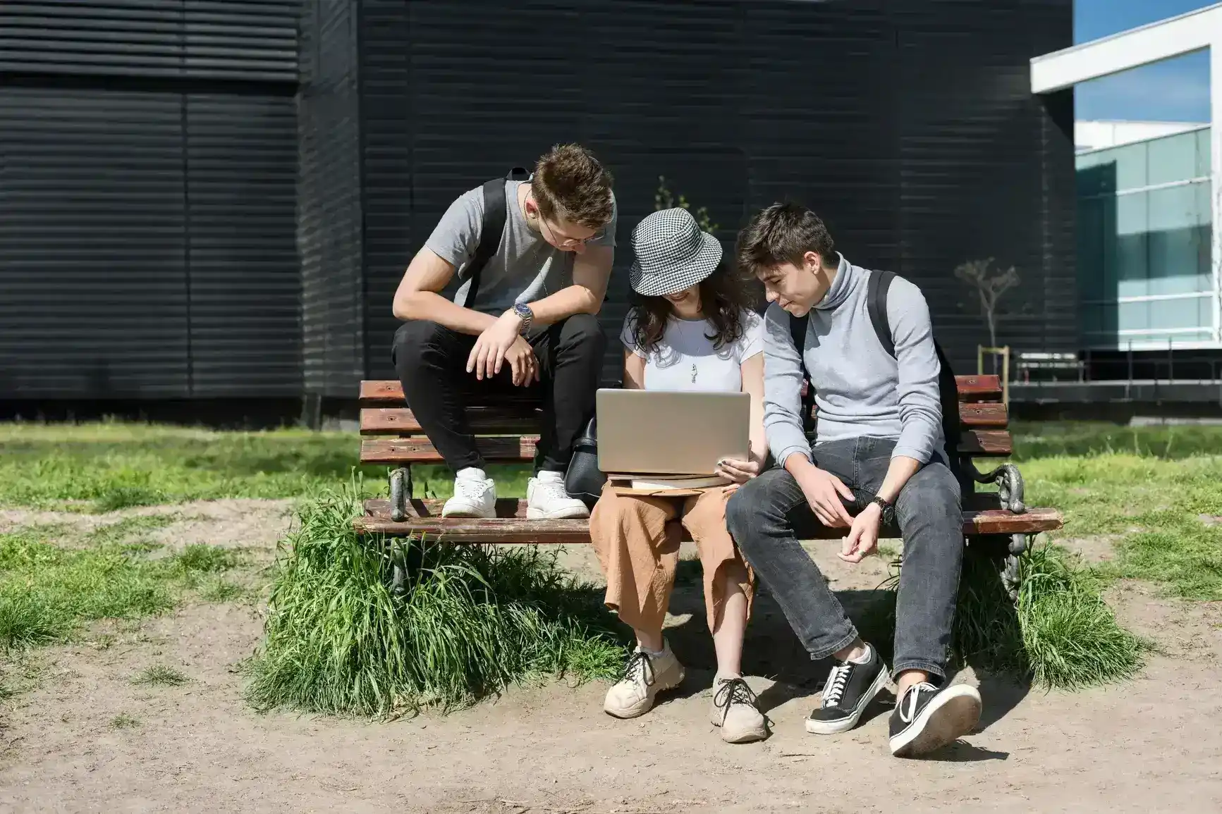 Three people sit on a bench and look into a laptop together.