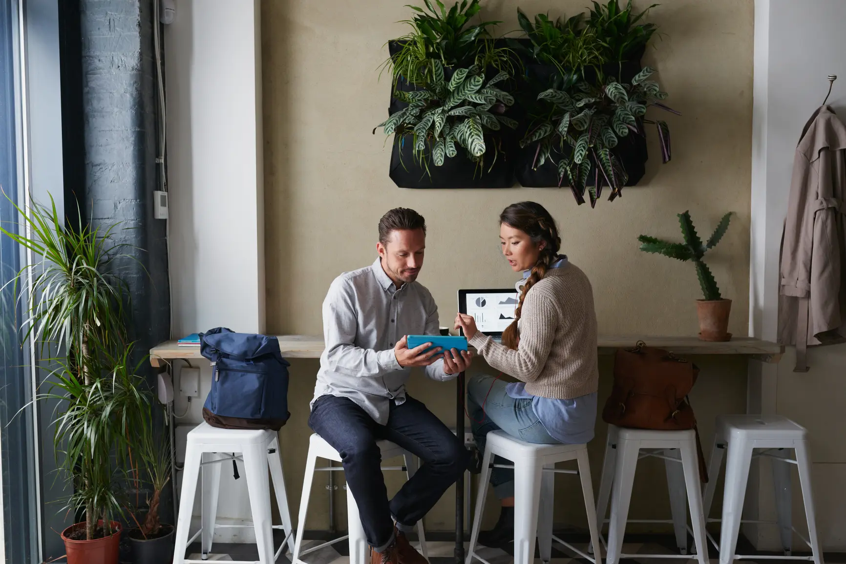 Zwei junge Unternehmer evaluieren Kennzahlen und Statistiken in einem modernen Cafe.