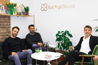 Luc Mader is sitting on a sofa and couch with two colleagues. All three look into the camera.