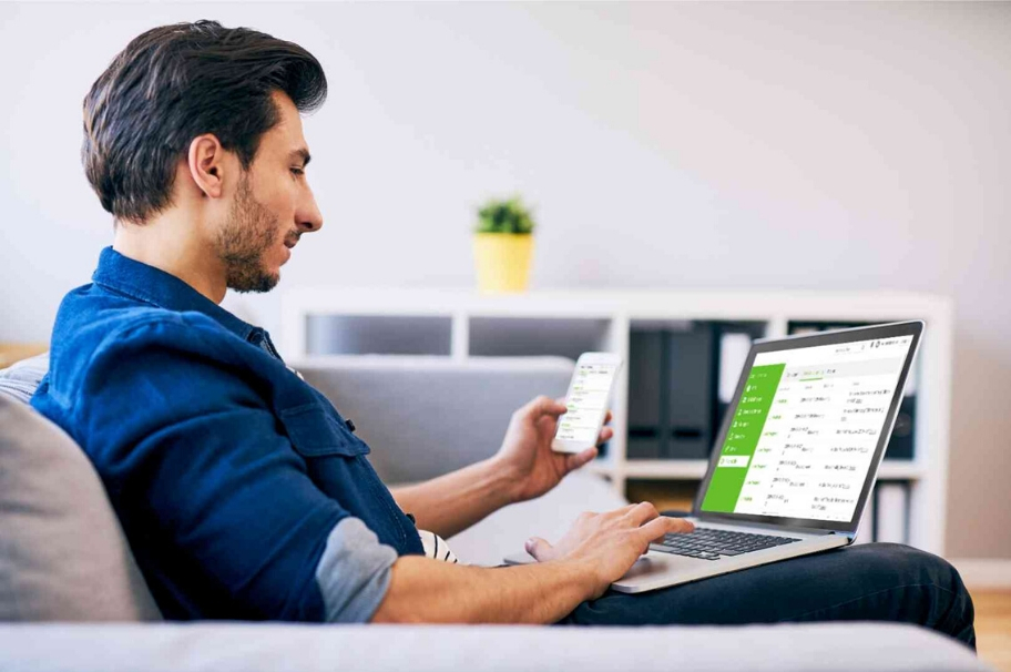 A man is sitting on a sofa working on a laptop and smartphone. On both devices luckycloud is open