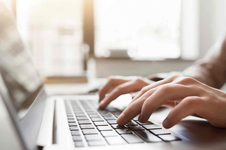 Close-up on the keyboard of a laptop. Two hands are typing on this