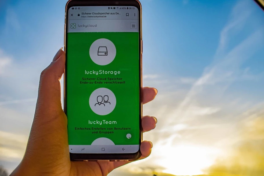 A smartphone is held aloft - the luckyStorage can be seen on the screen, with a sunrise in the background.