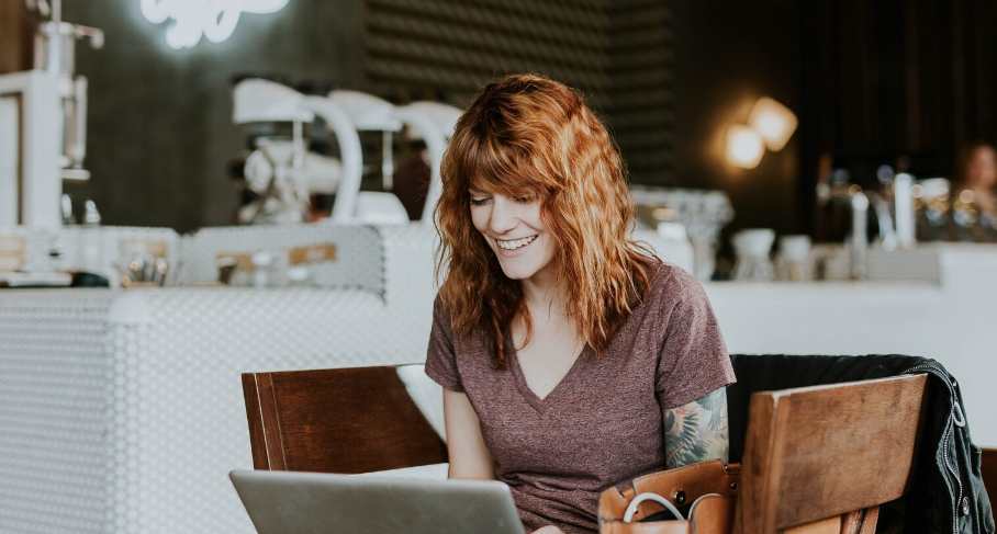 A woman sits in front of her laptop at her desk and laughs lightly