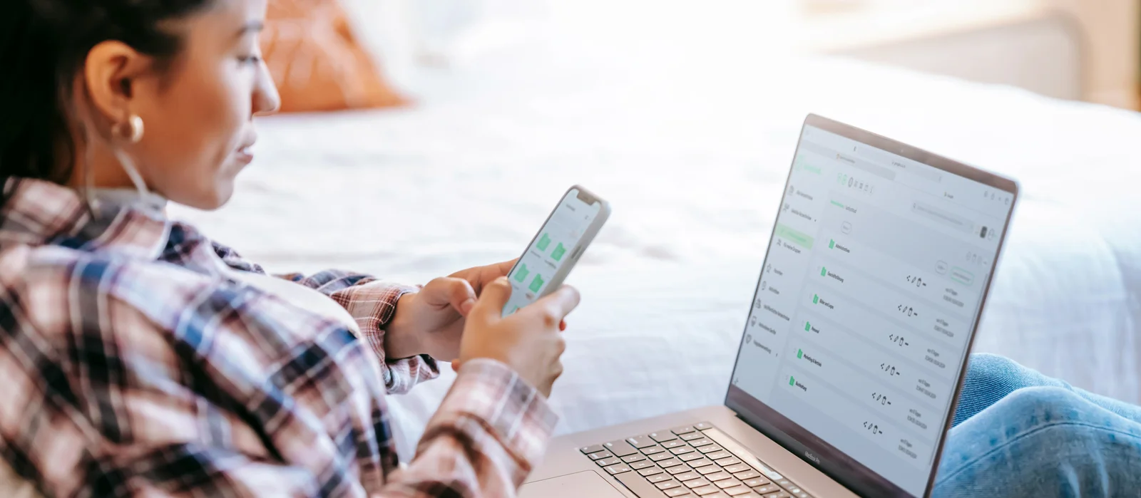 A young woman looks at a smartphone and a notebook with the luckycloud Android app open.