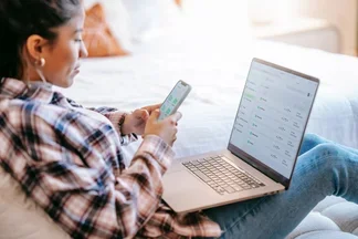 A young woman looks at a smartphone and a notebook with the luckycloud Android app open.