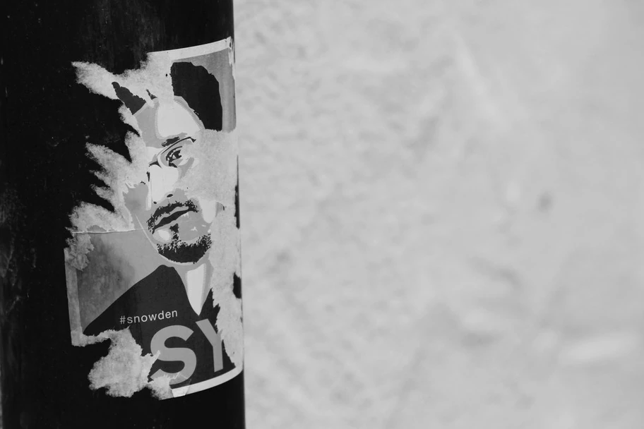 Schwarz-weiß Bild: Auf einer Saeule klebt ein Bild von Snowden, das bereits leicht zerrissen ist.