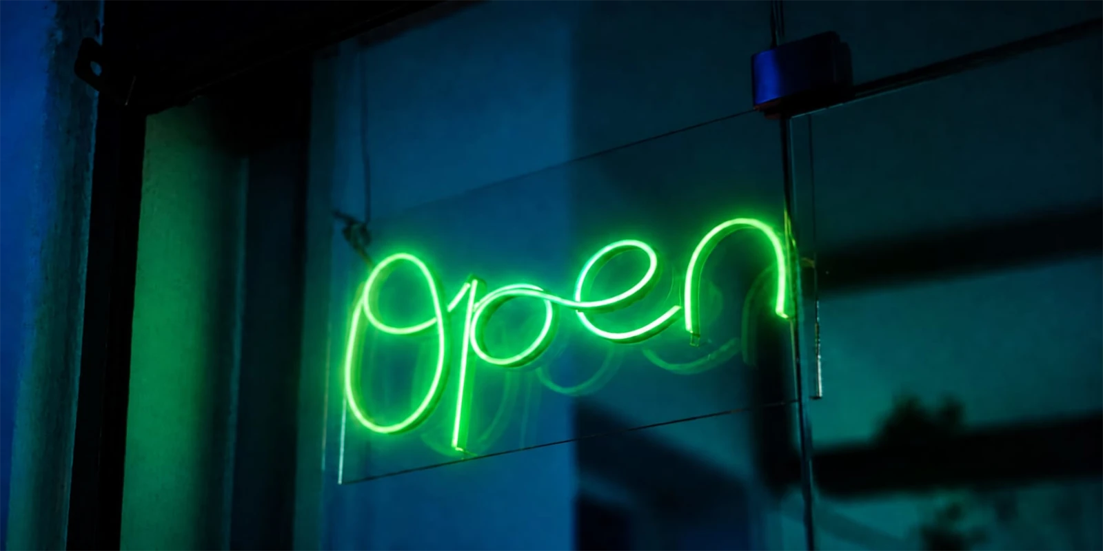 Green glowing neon sign reading “Open” hanging in a dark shop window, symbolizing luckycloud’s open source cloud.