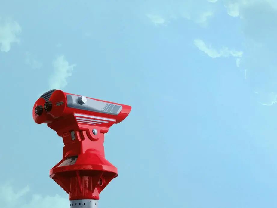 A pair of red binoculars stands in front of a blue sky.