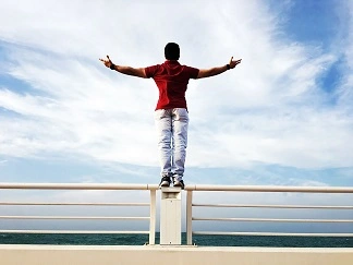 Man standing on the railing of a ship with his arms outstretched