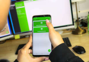 A woman holds a smartphone in her hand, behind her is a computer. On both screens luckycloud is open