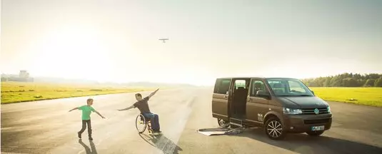 Ein Mann im Rollstuhl tobt mit seinem Sohn vor einem Fahrzeug, das behindertengerecht umgebaut wurde.